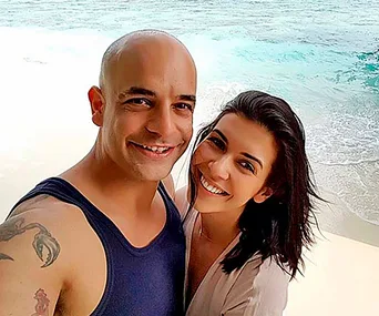 Two people smiling on a beach with waves in the background.