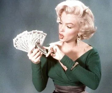 Person in green dress holding and counting a fan of dollar bills against a neutral background.