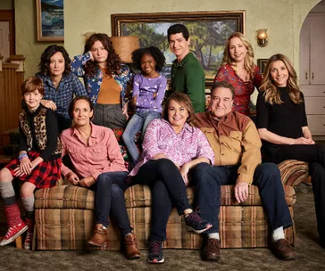 Cast of "The Conners" sitcom poses together on a couch in a living room setting.