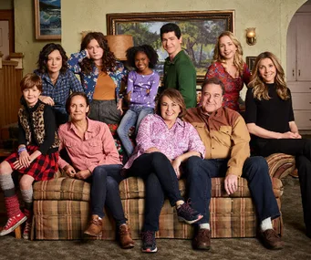 Cast of "The Conners" sitcom poses together on a couch in a living room setting.