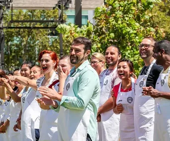 "MasterChef Australia contestants stand outside, wearing aprons and smiling, engaging in a group activity."