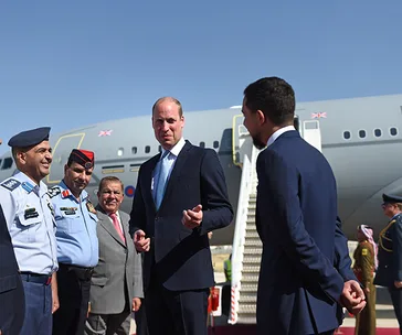 A group of men in formal attire stand beside an aircraft, conversing under a clear blue sky.