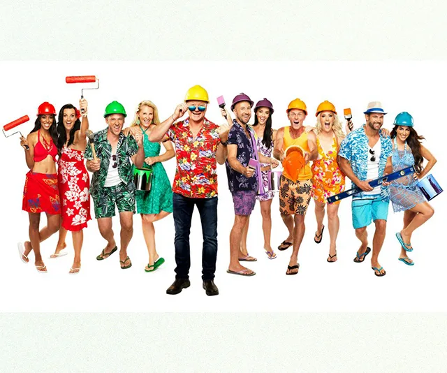 Contestants from The Block 2018 in colorful outfits and hard hats, holding painting tools, posing enthusiastically.