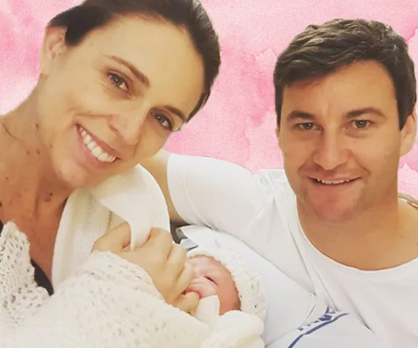 Family smiling warmly at the camera with their newborn wrapped in a blanket.