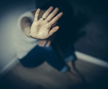 A person with a raised hand in a stop gesture, implying defense or refusal, sitting in a dimly lit setting.