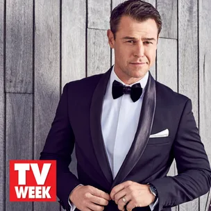 Man in a tuxedo adjusting his suit in front of a wooden wall, with a TV WEEK logo at the bottom corner.