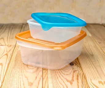 Stacked plastic containers with orange and blue lids on a wooden surface.