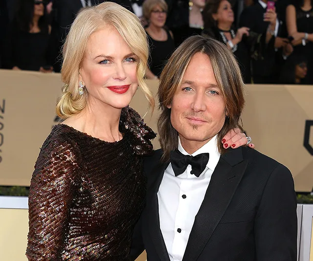 A couple posing elegantly on a red carpet, the woman in a dark sequined dress and the man in a formal suit.