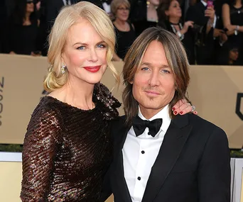 A couple posing elegantly on a red carpet, the woman in a dark sequined dress and the man in a formal suit.