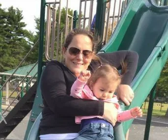 Image of young girl going down slide on her mother's lap