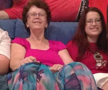 Two women sitting on a couch, smiling, wearing colorful clothing.