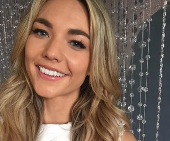 A woman with long blonde hair smiles in front of a crystal bead curtain.
