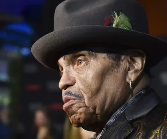 A man wearing a hat with a feather, seen in profile, at a formal event.