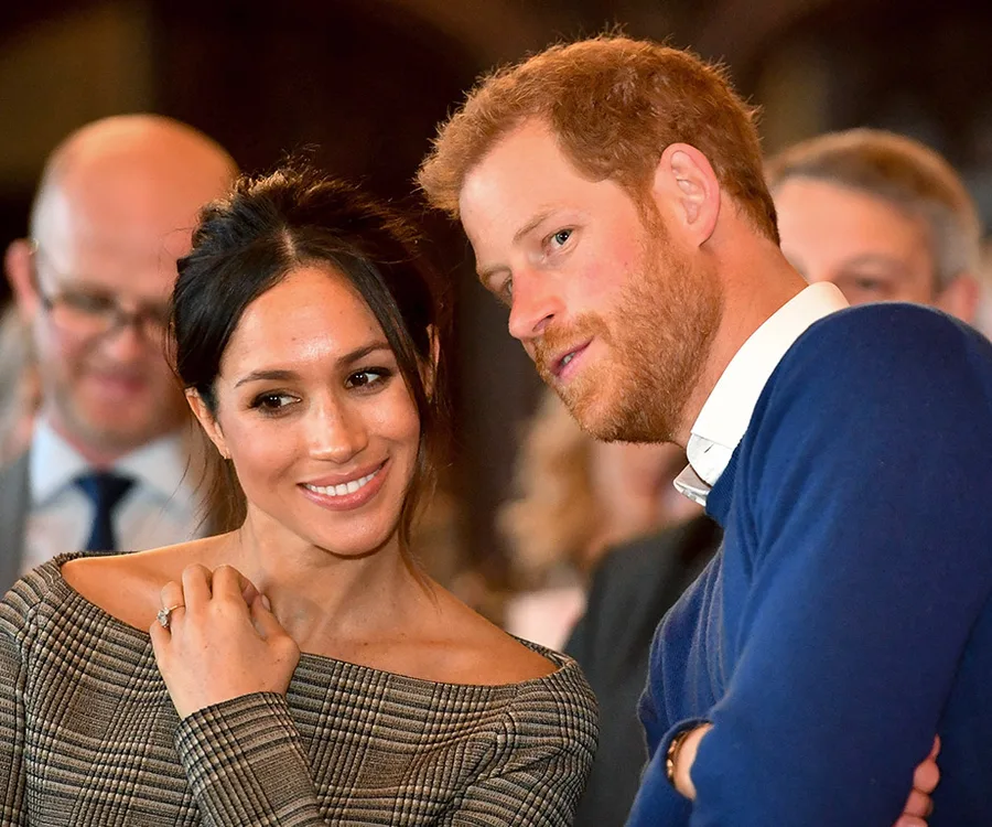 Prince Harry and Meghan Markle smiling and leaning close together at a public event.