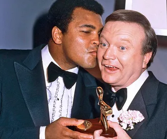 Bert Newton and Muhammad Ali at the 1979 Logies, with Ali playfully kissing Newton on the cheek, both in tuxedos.