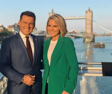 Two people smiling in front of London's Tower Bridge on a sunny day.