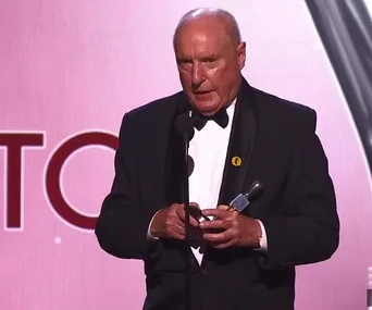 Ray Meagher in a tuxedo on stage holding a Logie award, making a dedication speech.