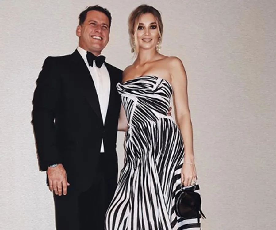 Man in a tuxedo and woman in a black and white striped dress posing together, smiling.