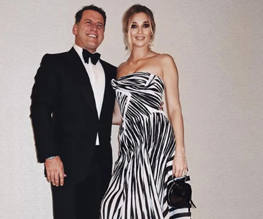 Man in a tuxedo and woman in a black and white striped dress posing together, smiling.