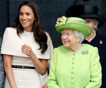 Two women smiling together, one in a cream outfit and the other in a bright green dress and hat.