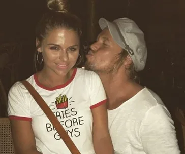 Woman in a "Fries Before Guys" t-shirt, with a man in a hat leaning in to kiss her cheek.