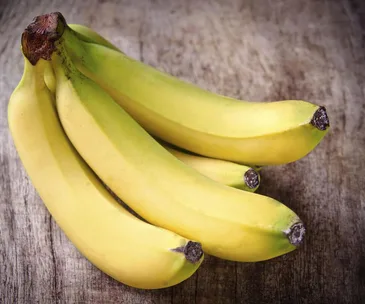 A bunch of ripe yellow bananas on a wooden surface.