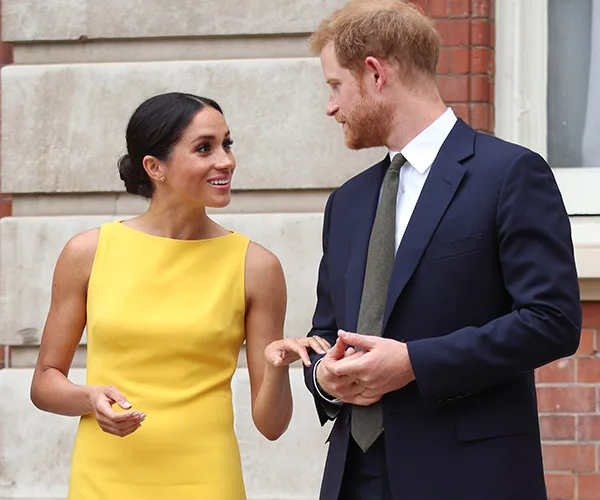 A woman in a bright yellow dress stands outdoors talking to a man in a dark suit, both smiling warmly.
