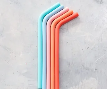 Colorful reusable straws in pastel shades, bent at the top, against a light textured background.
