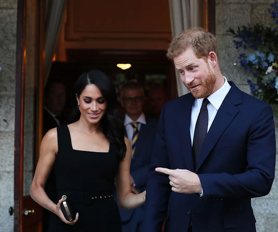 Meghan Markle and Prince Harry smiling and chatting at an event, both dressed formally.