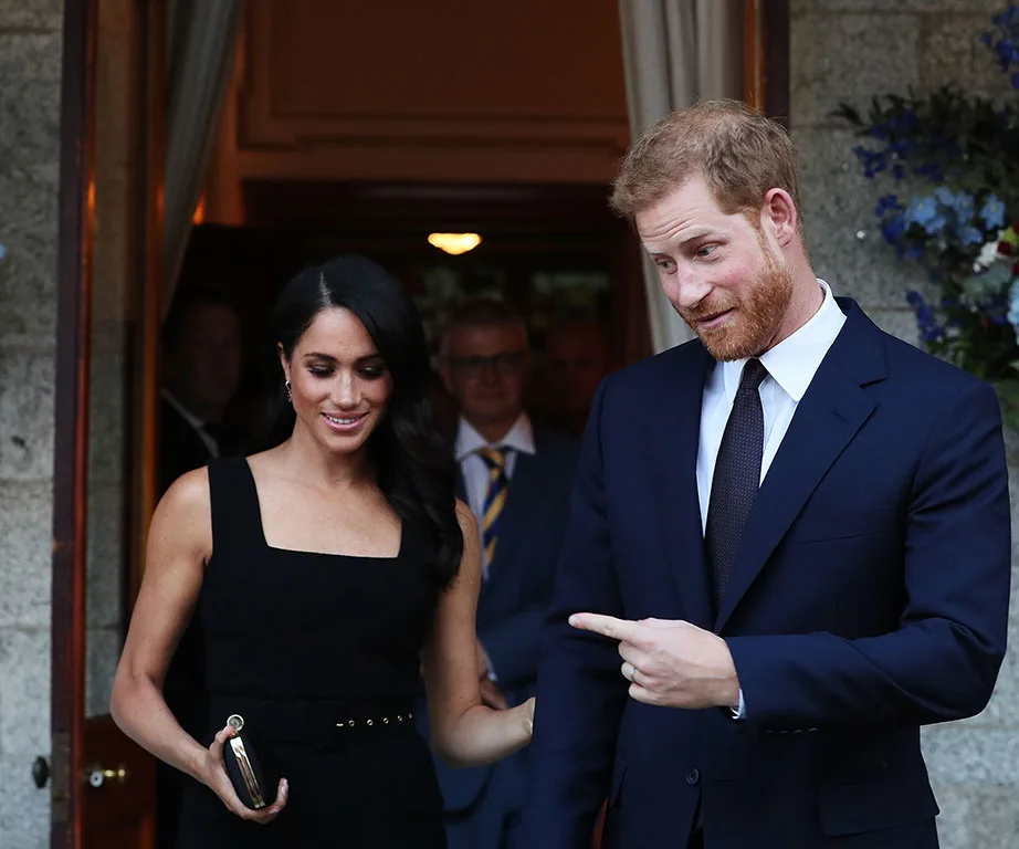 Meghan Markle and Prince Harry smiling and chatting at an event, both dressed formally.