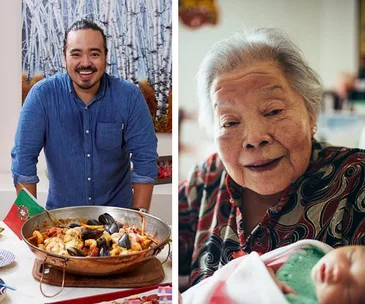 A man in a blue shirt stands by a seafood dish; an elderly woman smiles next to him, holding a baby.