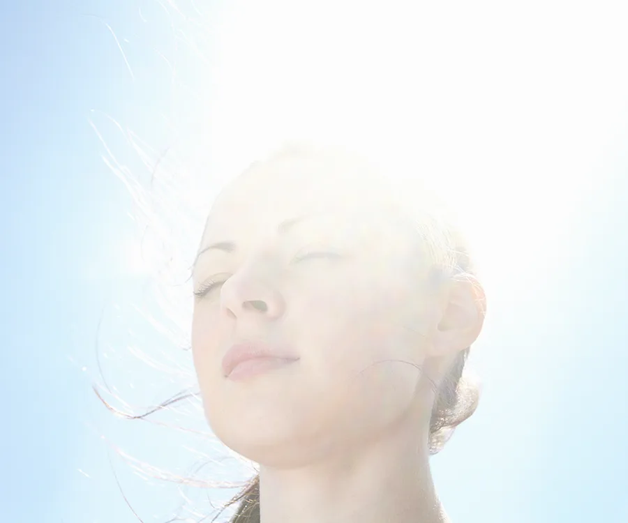 A person with closed eyes faces sunlight, suggesting serenity and meditation.