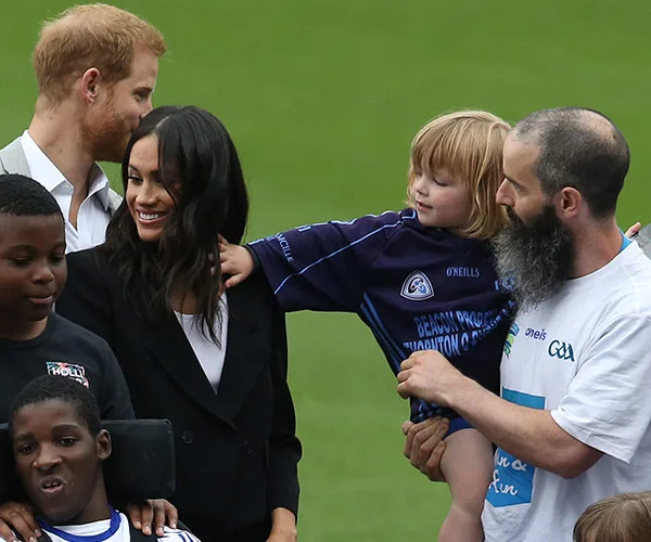 Toddler playfully pulls woman's hair while others, including a bearded man, laugh during a public event.
