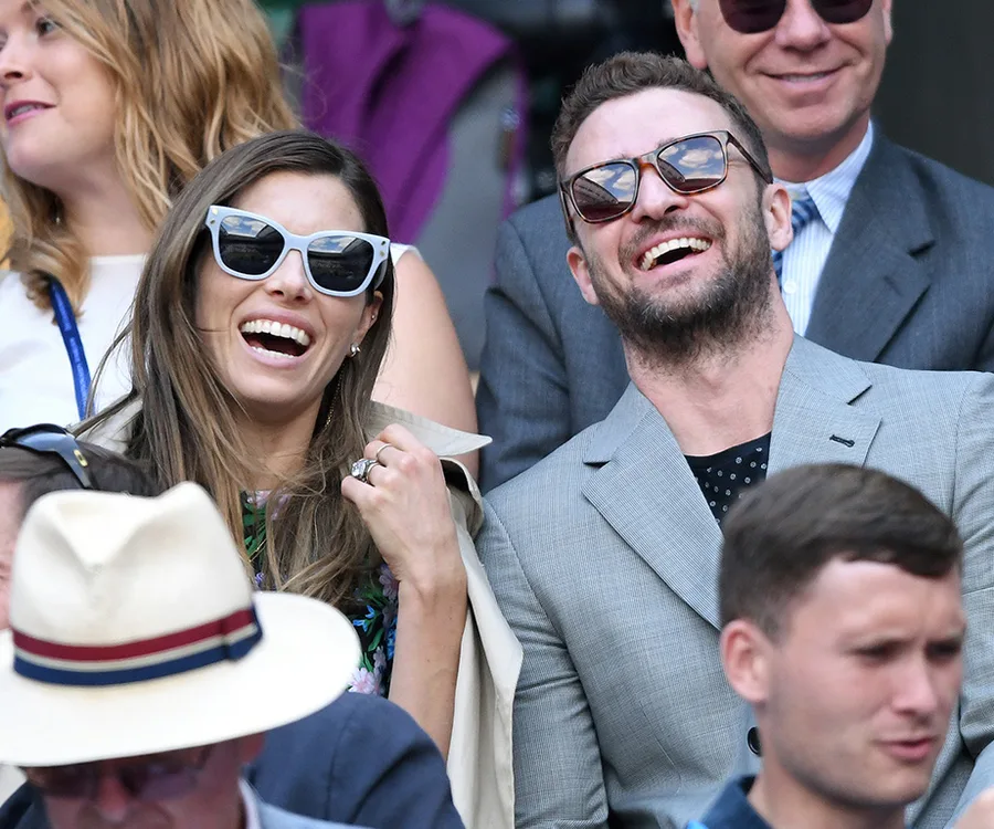 Sunglass-wearing couple laughing joyfully in the stands at Wimbledon 2018.