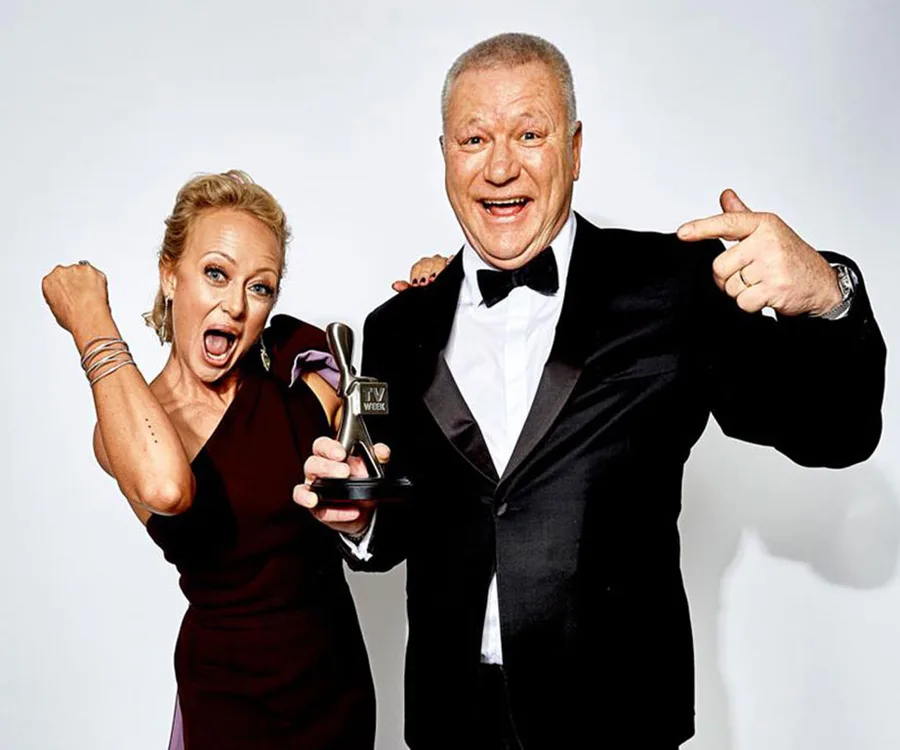 Two people celebrating, one holding an award. They are dressed formally and appear excited.