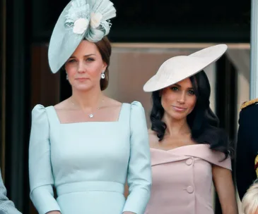 Two women at a formal event, wearing elegant dresses and hats, standing side by side.