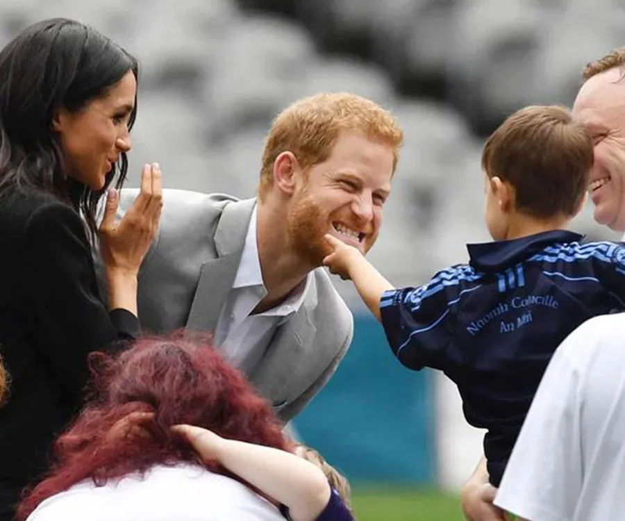 A smiling man interacts playfully with a child, while a woman watches and smiles in a public setting.