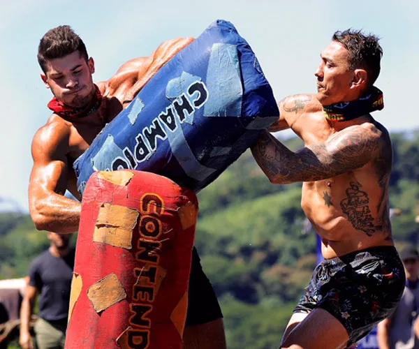 Two men from 'Australian Survivor' 2018 face off in a physical challenge holding padded obstacles labeled "Champions" and "Contenders".