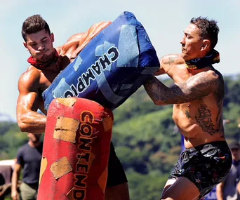 Two men from 'Australian Survivor' 2018 face off in a physical challenge holding padded obstacles labeled "Champions" and "Contenders".