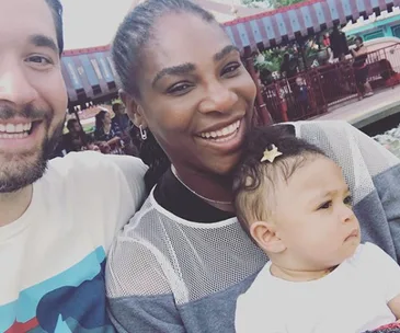 A family enjoying their day at an amusement park, smiling, holding a baby with a star hair clip.
