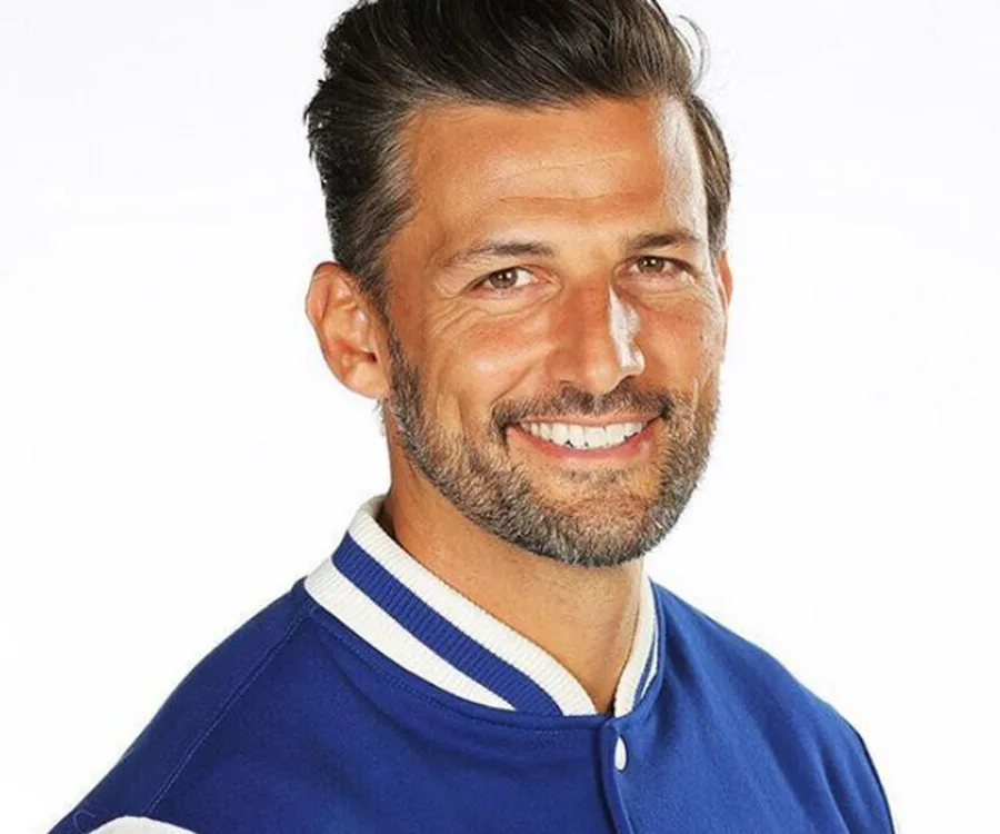 Smiling man in a blue and white jacket against a plain background.