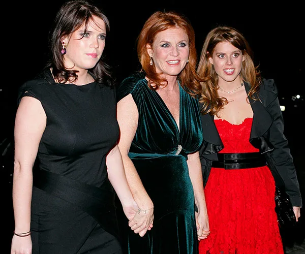Sarah Ferguson with her daughters, wearing formal black and red dresses, smiling and holding hands at an evening event.