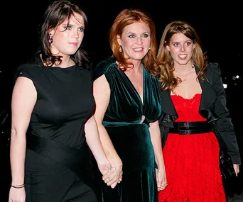Sarah Ferguson with her daughters, wearing formal black and red dresses, smiling and holding hands at an evening event.