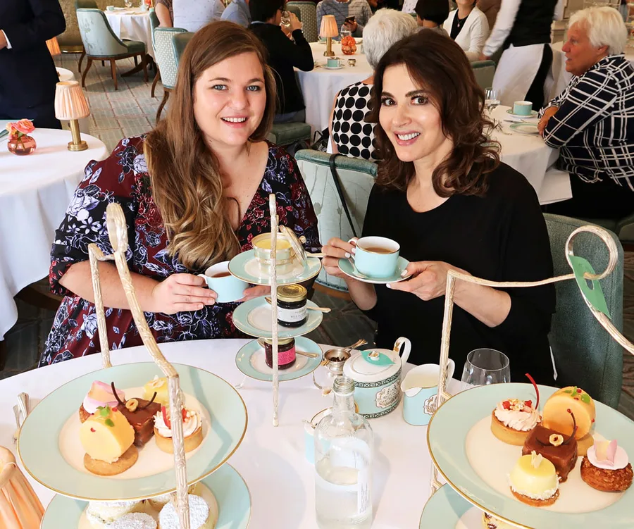 Two women enjoying afternoon tea with pastries on a tiered stand in an elegant setting.