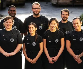 A group photo of MasterChef Australia 2018 contestants, wearing black aprons with name tags, smiling outdoors.