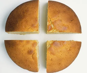 A round sponge cake cut into four equal pieces on a white background.