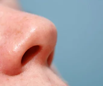 Close-up of a person's nose against a light blue background.