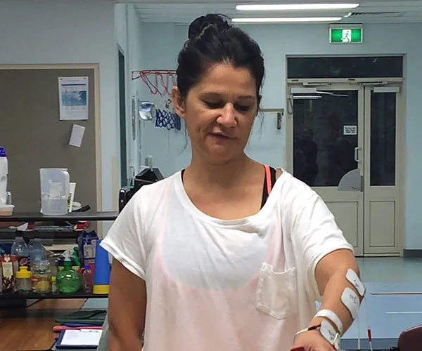 A woman in a physical therapy room uses electrodes on her arm, possibly for stroke rehabilitation exercises.