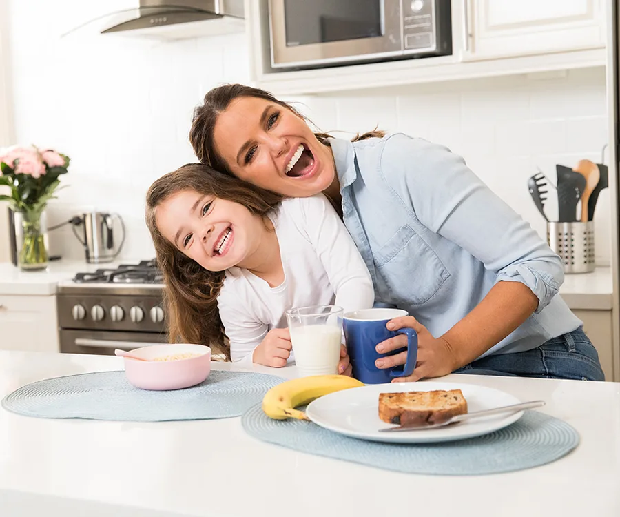 Mother and daughter smiling in a kitchen with breakfast items on the counter.