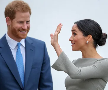 Prince Harry and Meghan Markle smiling and interacting, Meghan gesturing with her hand raised.